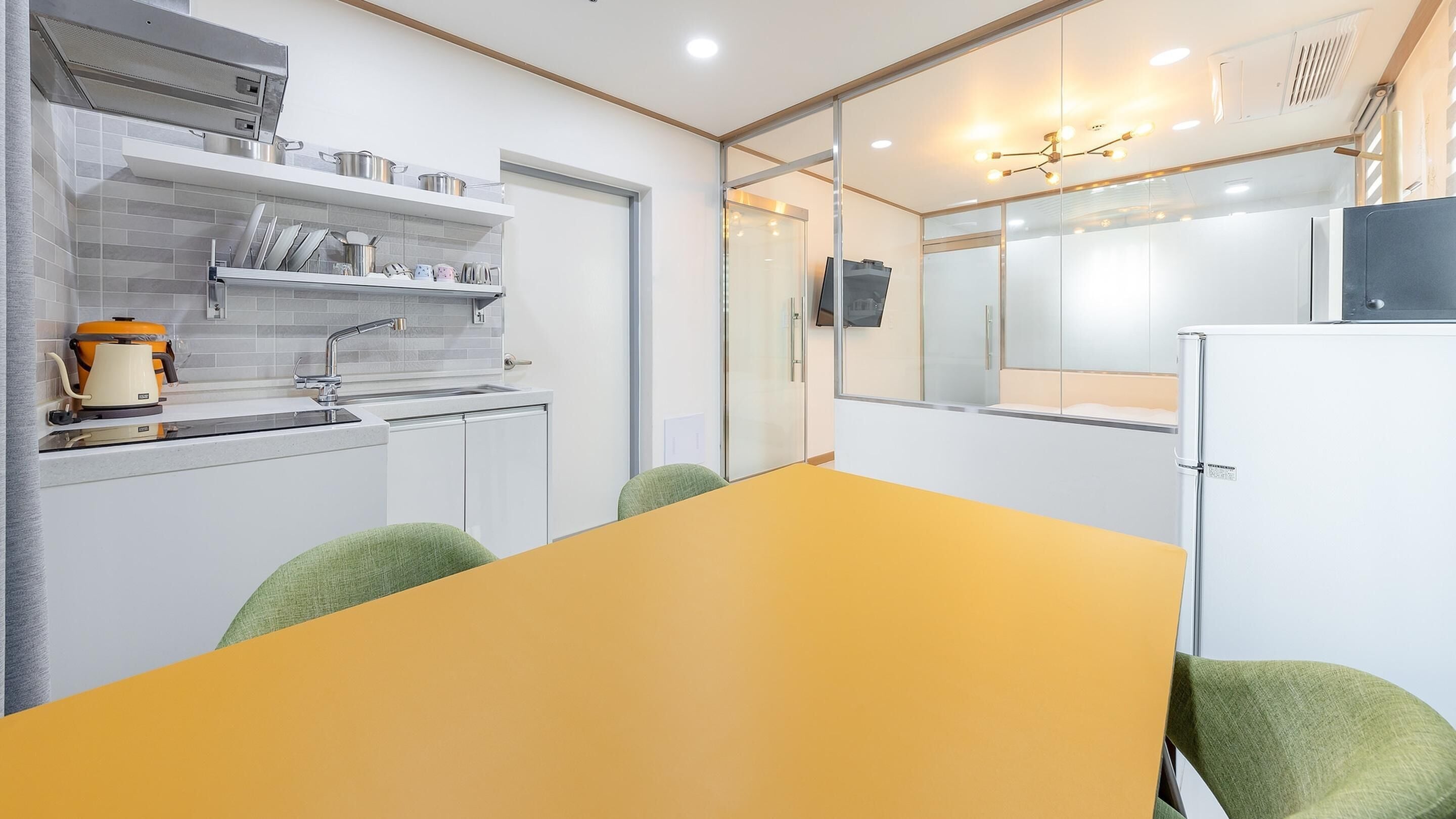 A modern kitchen with a yellow table, green chairs, and a white refrigerator.