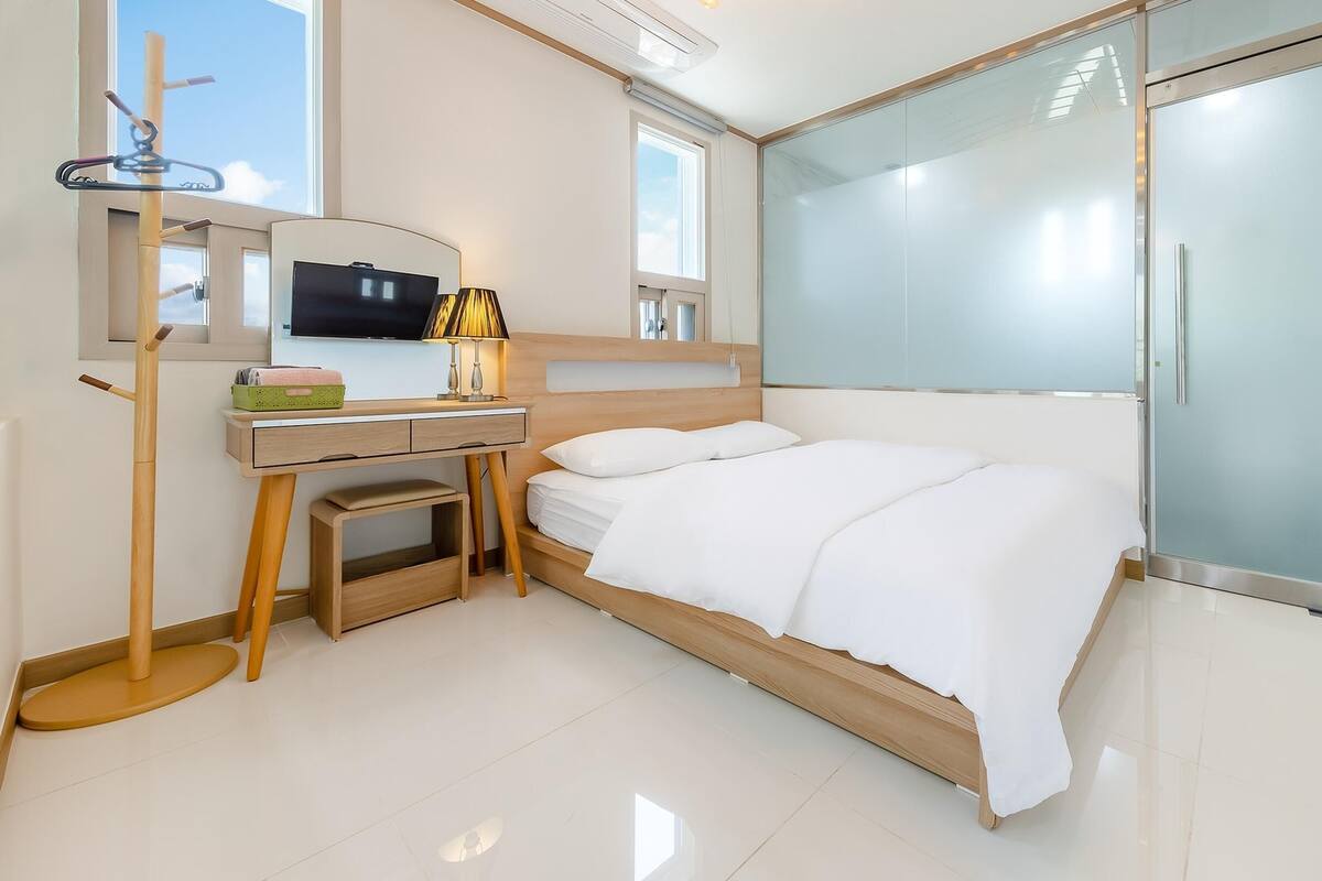 A modern bedroom with a bed, a desk, a chair, a TV, and a sliding glass door.
