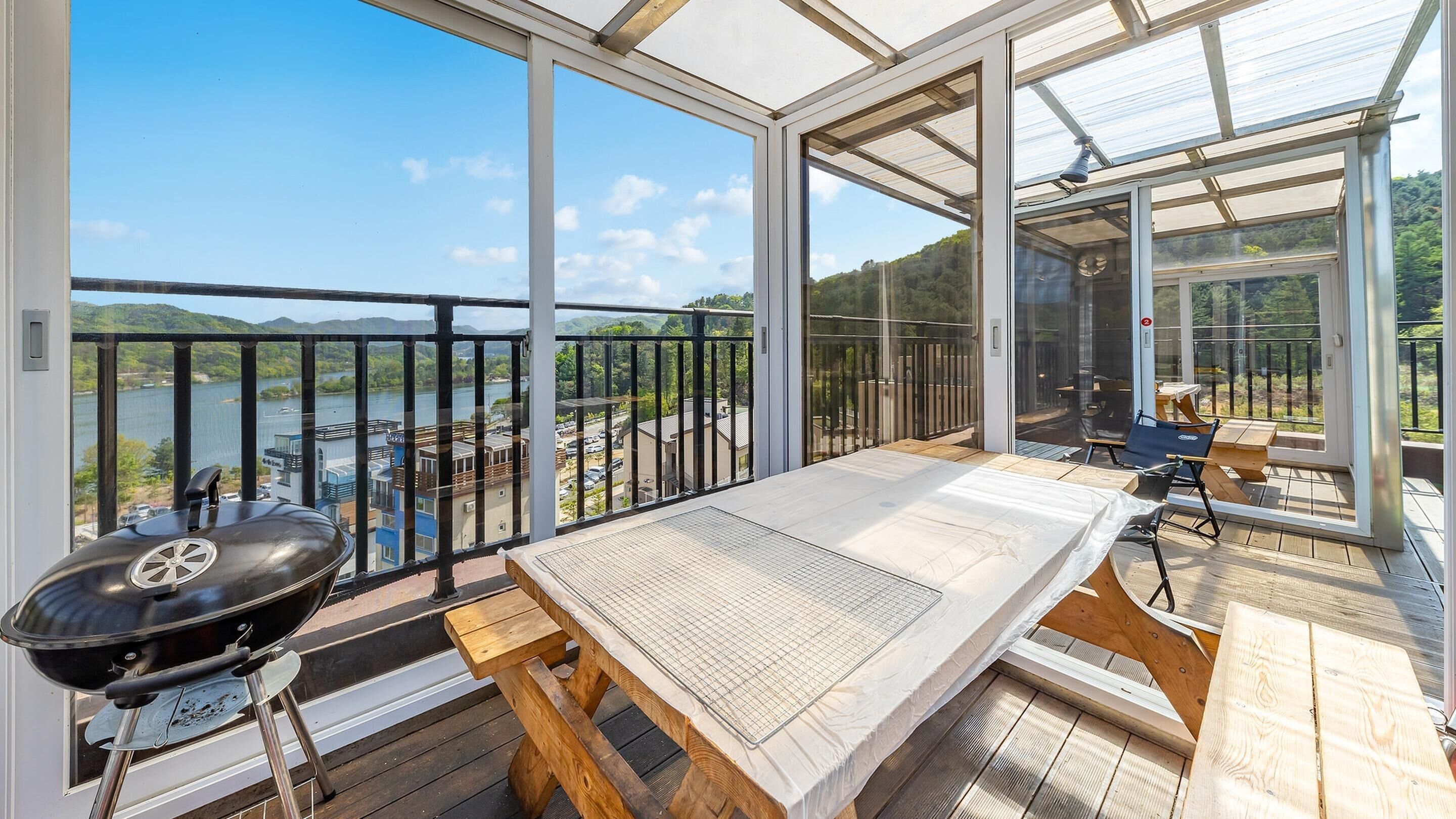 A balcony with a grill, a table, and a view of a lake and hills.