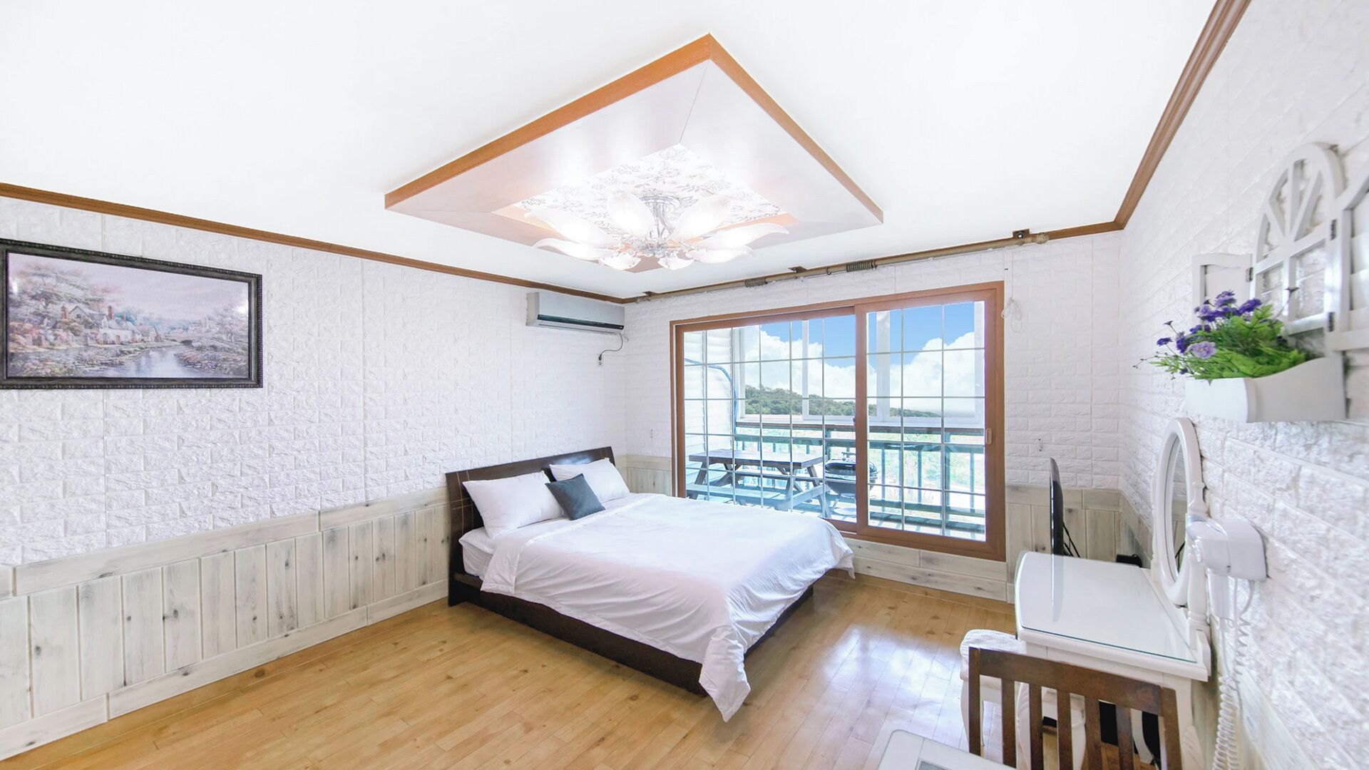 Une chambre à coucher avec un lit, une fenêtre, un tableau au mur et un luminaire au plafond.