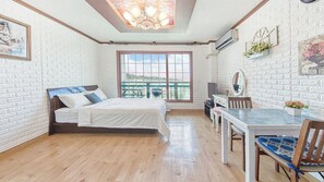 Ein Schlafzimmer mit Bett, Schreibtisch, Stuhl, Fenster mit Aussicht und einer Deckenleuchte.