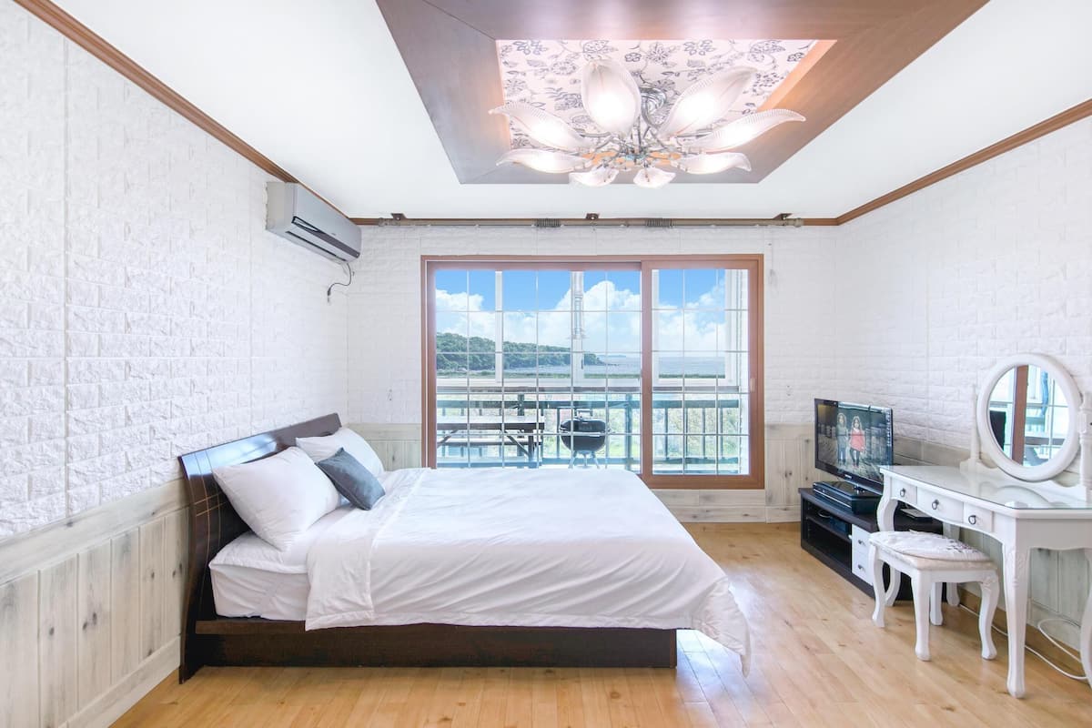 Ein Schlafzimmer mit einem großen Bett, einem Fernseher, einem Schminktisch mit Spiegel und einem Balkon mit Blick.