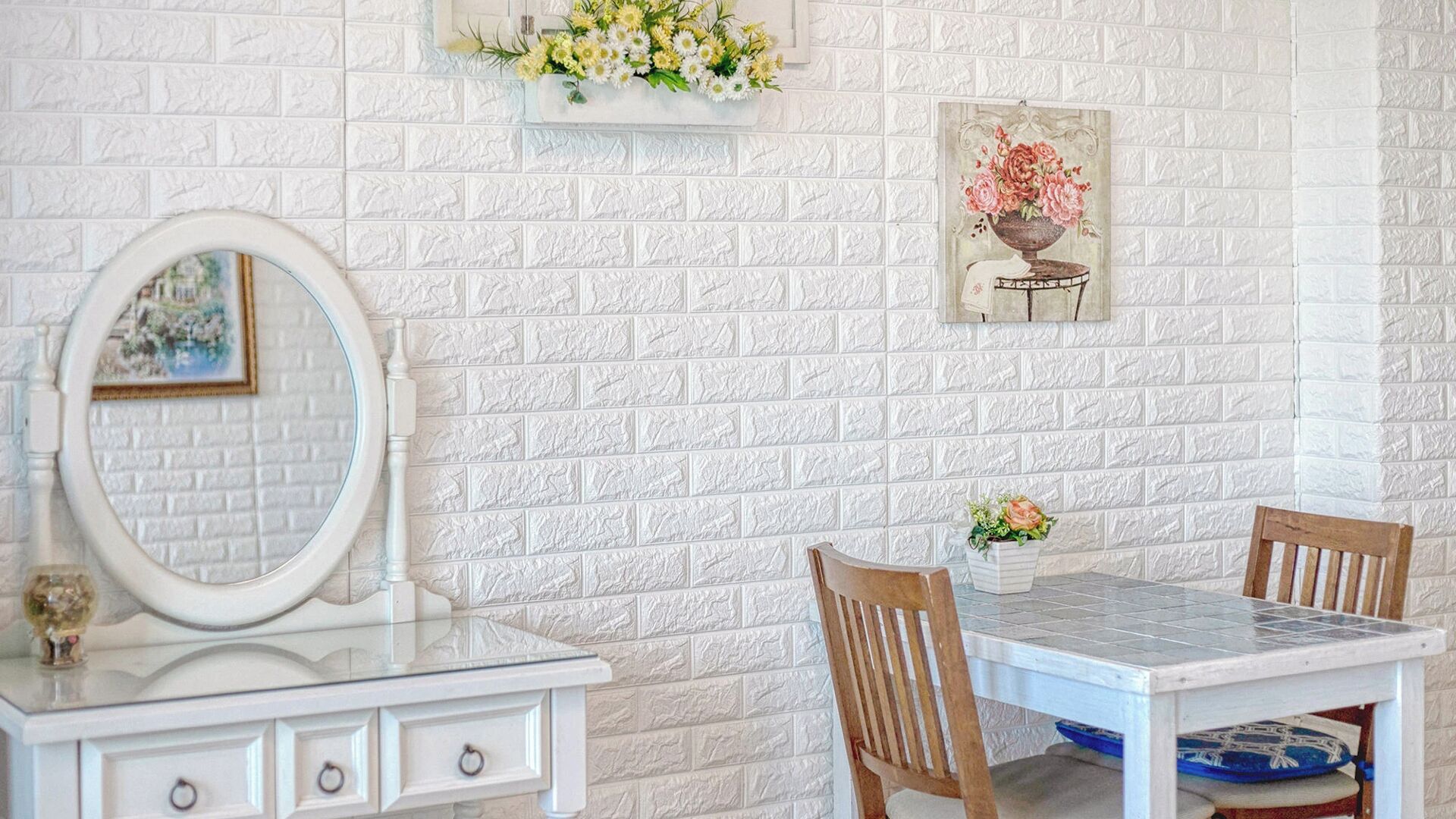 Una habitación con pared de ladrillo blanco, un aparador blanco con espejo, una mesita con sillas y un cuadro floral enmarco.