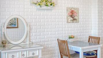 Una habitación con pared de ladrillo blanco, un aparador blanco con espejo, una mesita con sillas y un cuadro floral enmarco.
