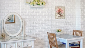 A room with a white brick wall, a white dresser with a mirror, a small table with chairs, and a framed floral painting. - Ganghwa Ara Pension (Incheon)