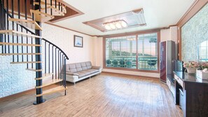 Ein geräumiger Wohnbereich mit einer Holztreppe, einem Sofa, einem großen Fenster mit Blick und einem Fernseher.