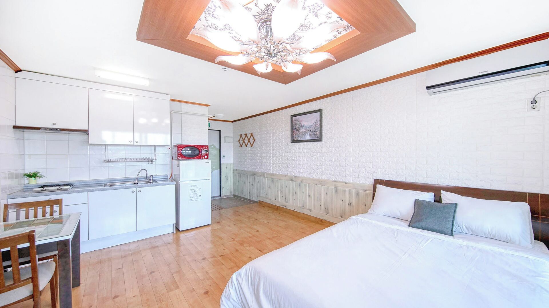 A hotel room with a bed, a small kitchenette, and a view of the hallway.