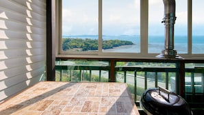 A balcony with a view of a body of water and a distant island, a metal grill, and a tiled floor. - Ganghwa Ara Pension (Incheon)