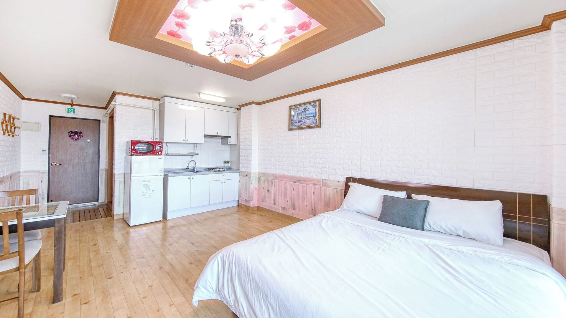 A bedroom with a large bed, a dining table, and a kitchenette in the adjacent room.