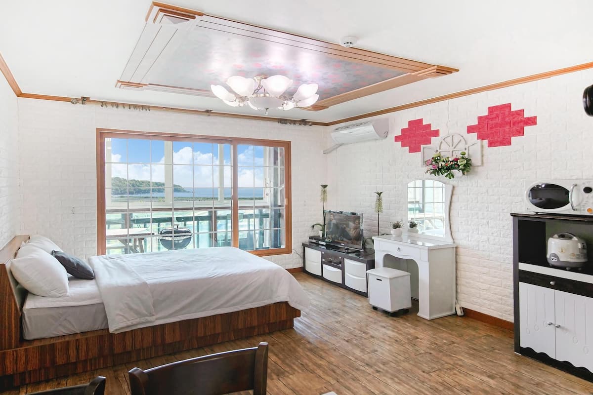 Ein Schlafzimmer mit einem großen Bett, einem Schminktisch, einem Fernseher und Meerblick durch ein großes Fenster.