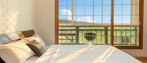 A bedroom with a large sliding glass door leading to a balcony with a barbecue grill.