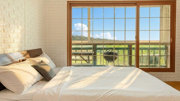 Ein Schlafzimmer mit einer großen Glasschiebetür, die auf einen Balkon mit einem Grill führt.