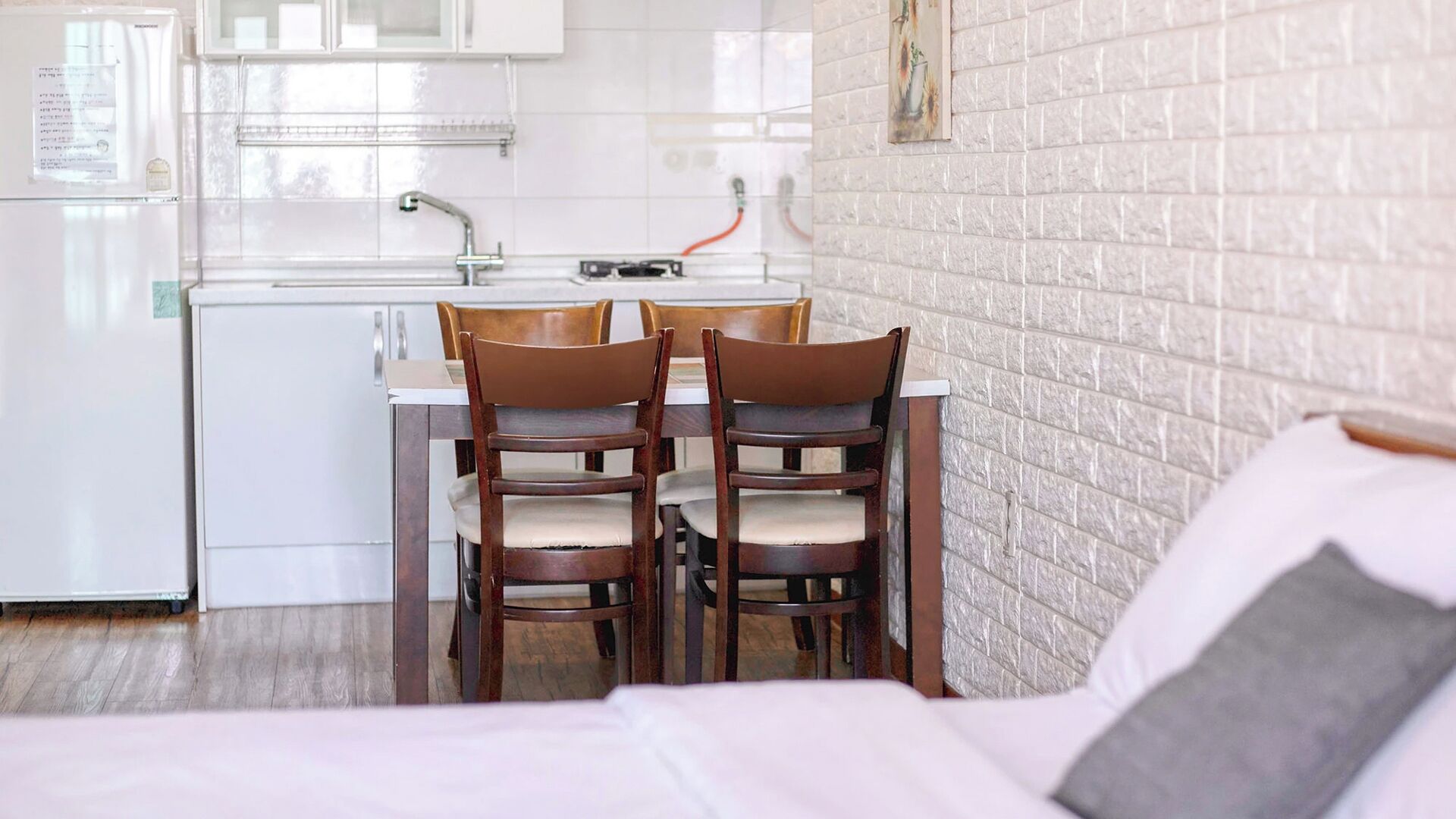 A compact kitchen with a dining area, a bed, and a brick wall.