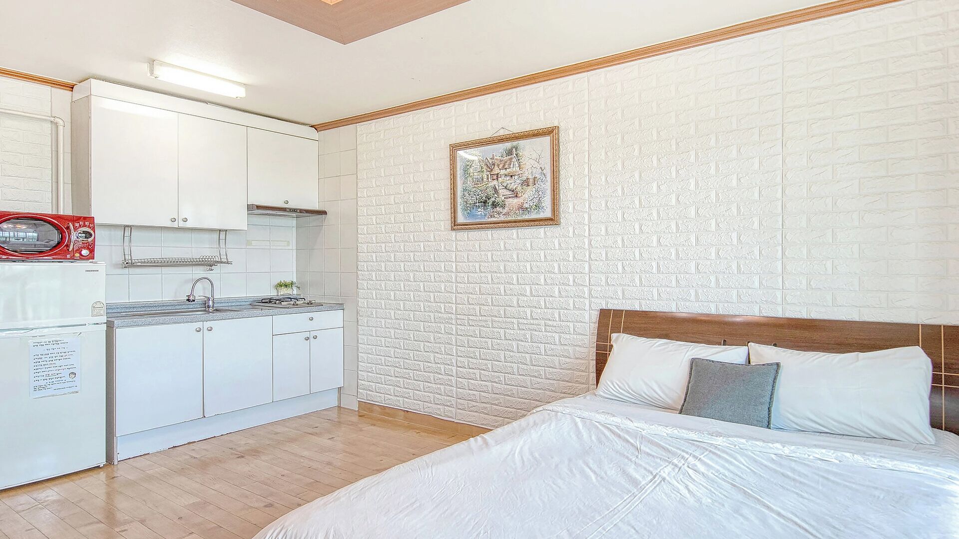 A compact room with a kitchenette, a bed with pillows, and a brick-patterned wall.