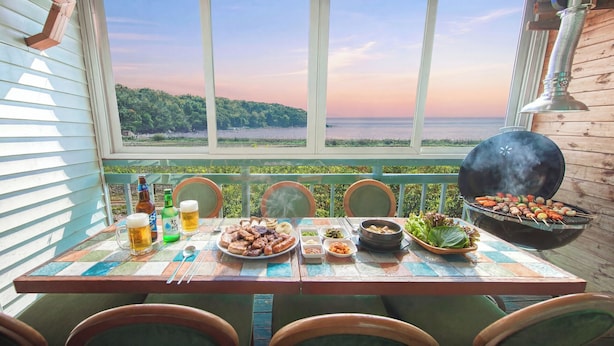 A table set for a meal with a view of the sea, a grill, and a bottle of beer. - Ganghwa Ara Pension (Incheon)