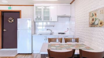 A modern kitchen with white cabinets, a refrigerator, a sink, and a dining table with chairs.