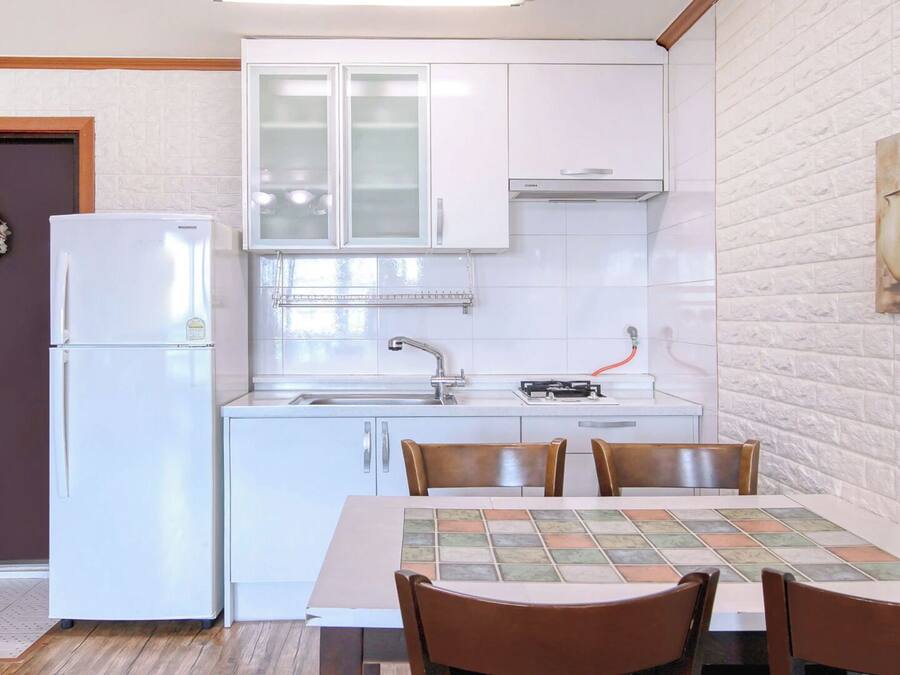A modern kitchen with white cabinets, a refrigerator, a sink, and a dining table with chairs.