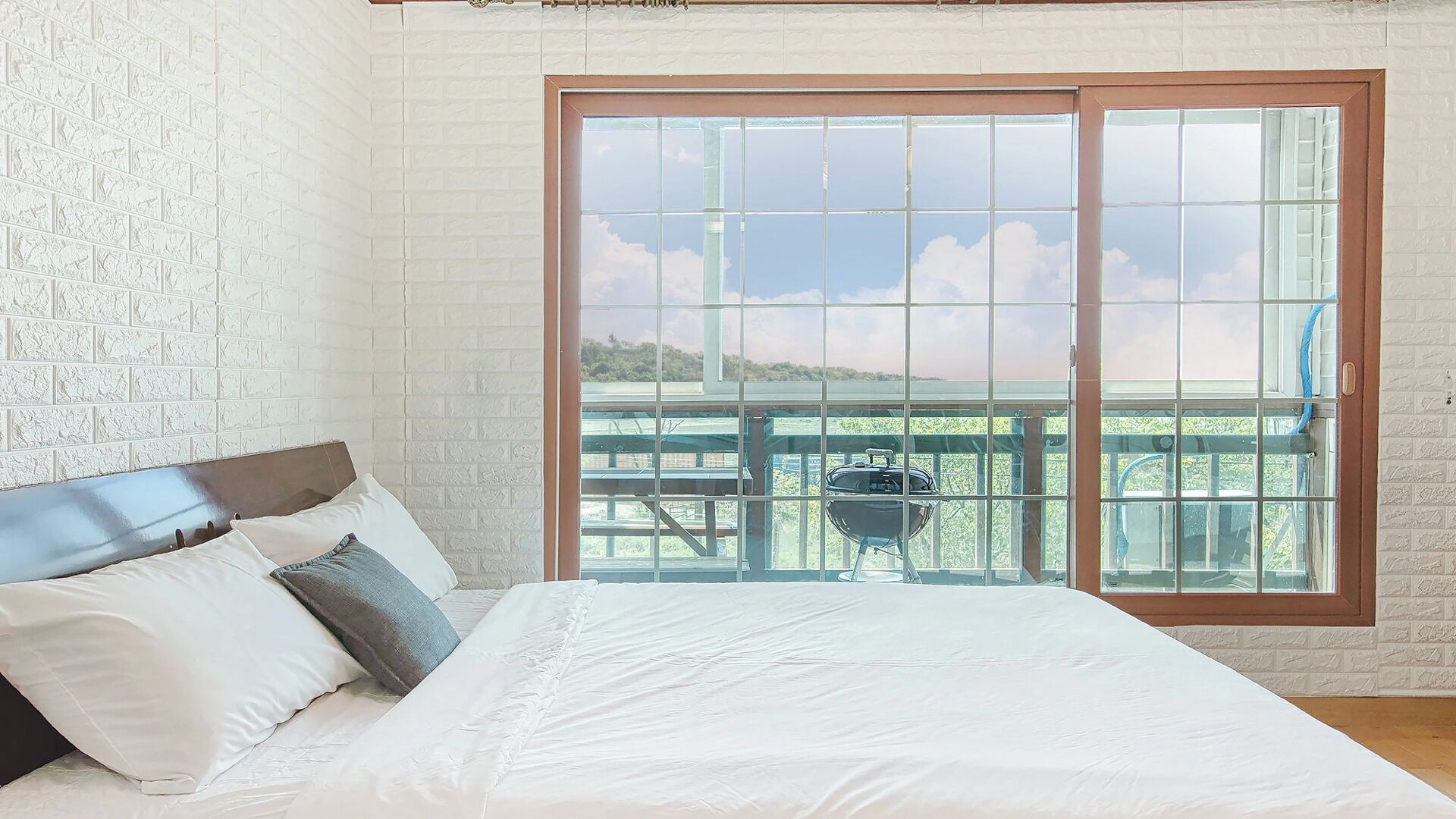 A bedroom with a large bed, a sliding glass door leading to an outdoor deck, and a white brick wall.