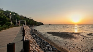 A coastal road with a stone wall and a metal railing, leading to a beach with calm waters and a sunset. - Ganghwa Ara Pension (Incheon)