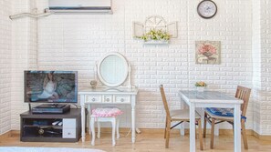 A room with a television, a dresser, a mirror, a dining table with chairs, and a clock on the wall.
