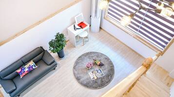 Un salon moderne avec un canapé, une petite table, une plante en pot, un tapis rond et une fenêtre avec des stores.
