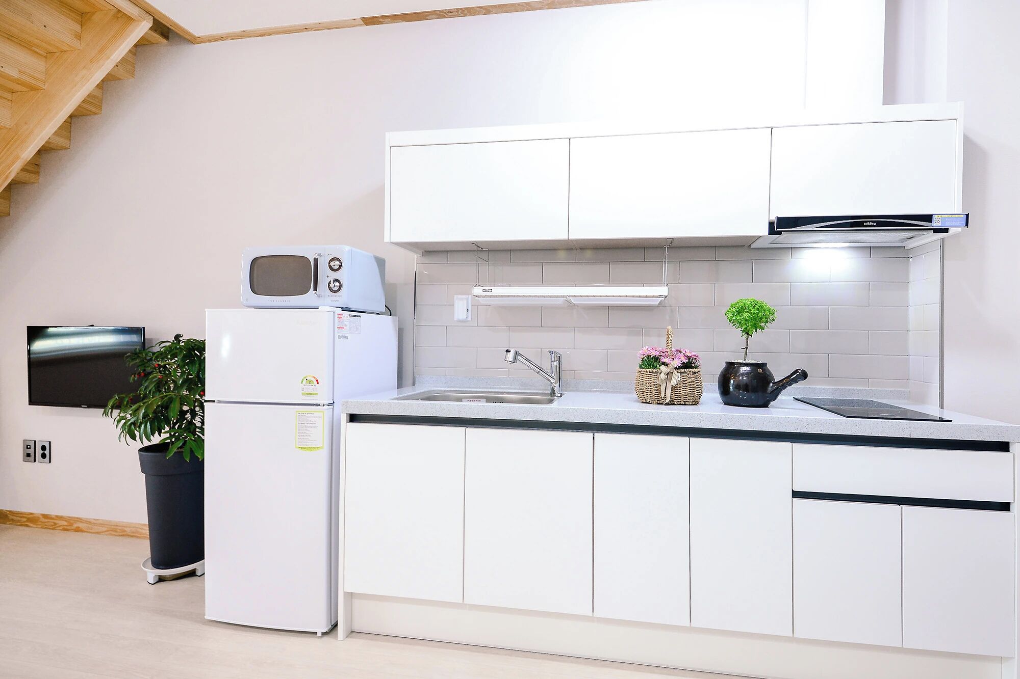A modern kitchen with white cabinetry, a microwave, a sink, and a small potted plant.