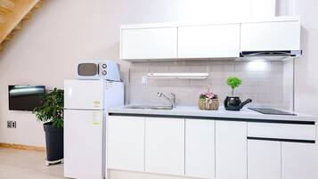 A modern kitchen with white cabinetry, a microwave, a sink, and a small potted plant.