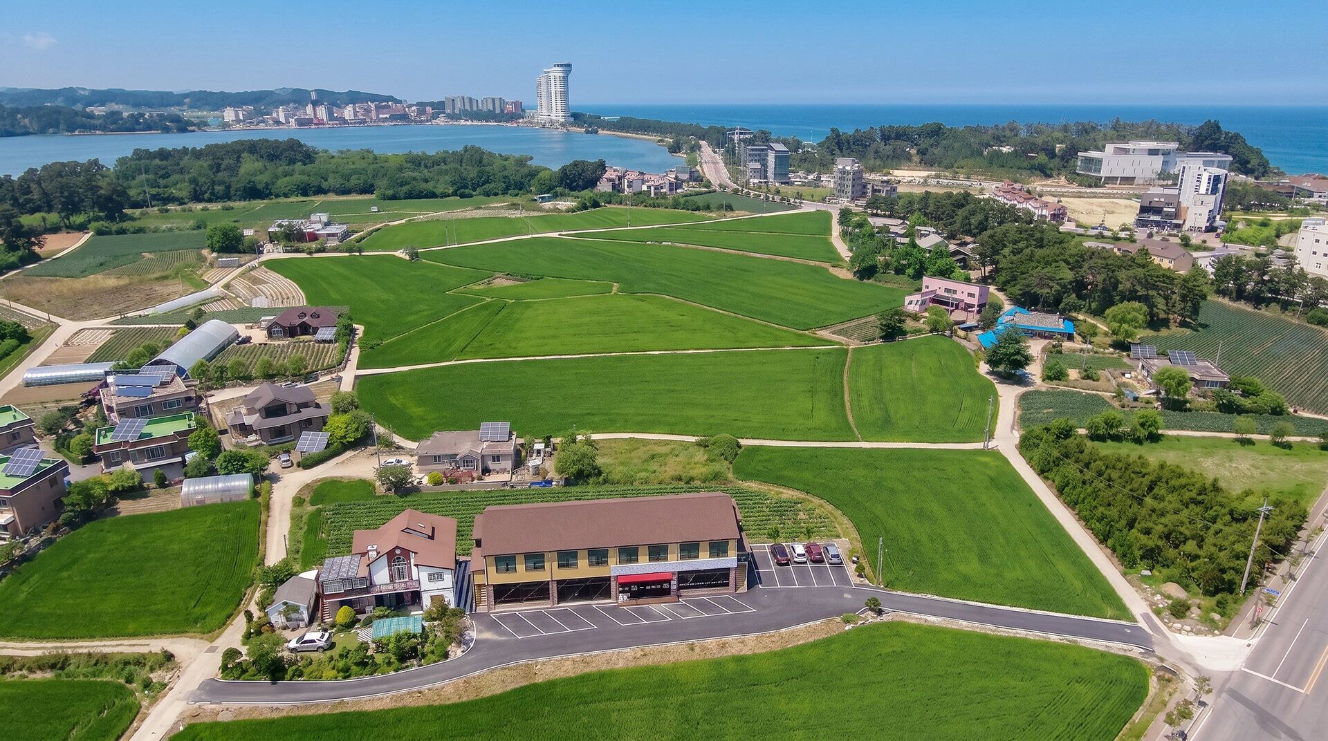An aerial view of a residential area with green fields, a parking lot, and buildings with solar panels.