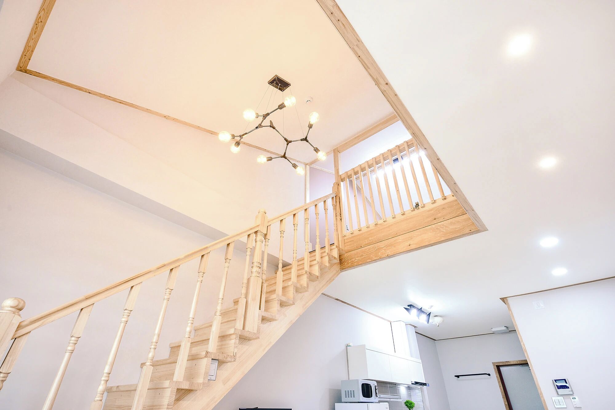 Ein modernes Interieur mit einer Holztreppe, einer Deckenleuchte und einem Küchenbereich.