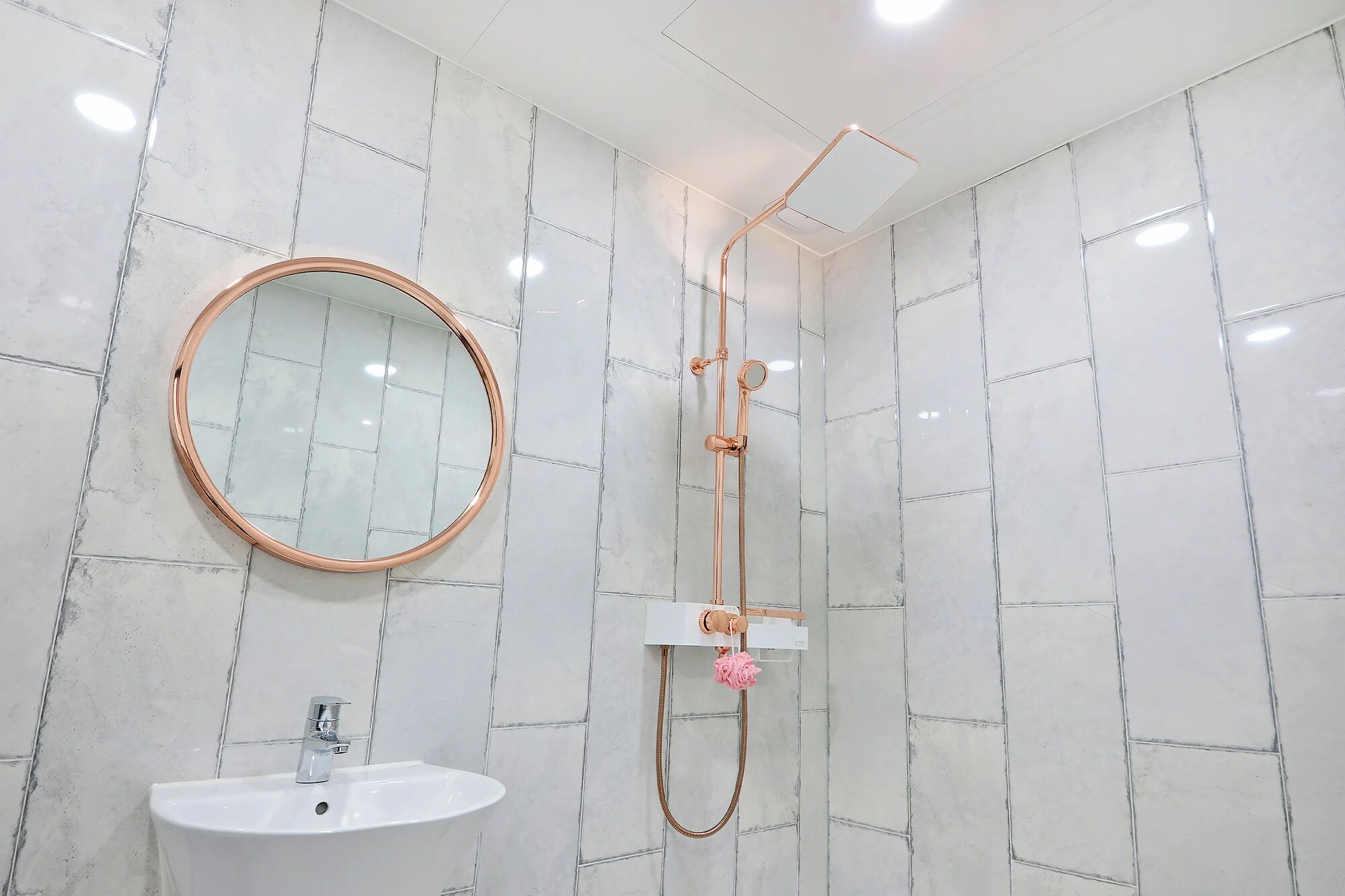 A bathroom with a white sink, a round mirror, and a shower with a rose decoration.