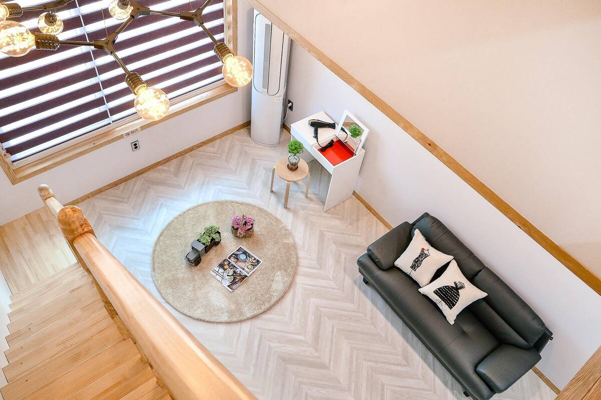 Een moderne woonkamer met een visgraatvloer, een rond vloerkleed, een zwarte bank en een plafondlamp.