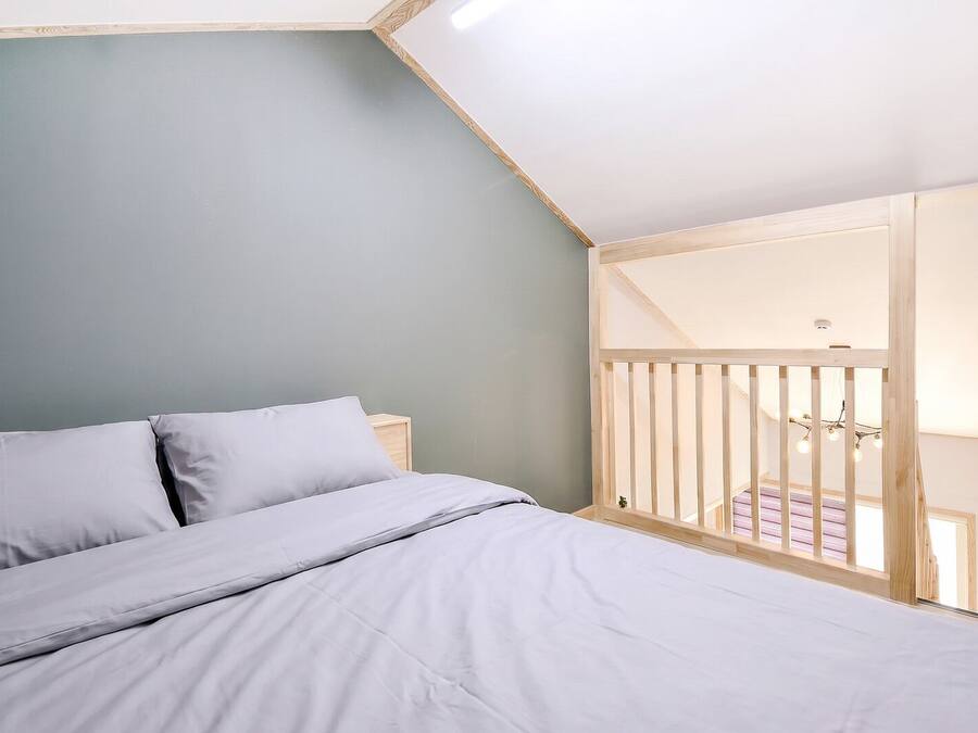 A bedroom with a bed, a wooden railing, and a view of a balcony.