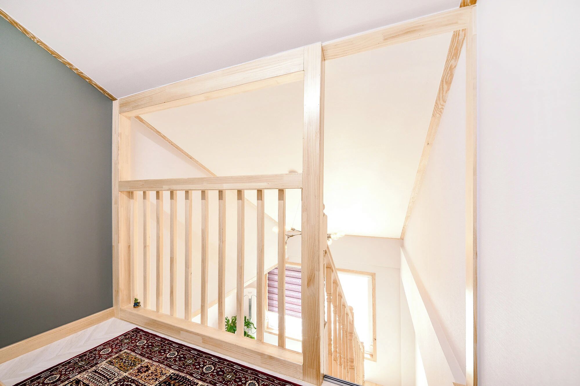Een kamer met een houten trap, een kamerbreed tapijt met patroon en uitzicht op een gebouw.