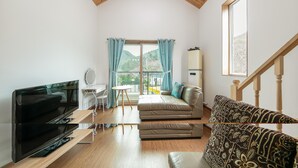 A modern living room with a flat-screen TV, a sofa, a patterned armchair, a small table, and a window with curtains. - Gapyeong Twelve Pension (Gapyeong)