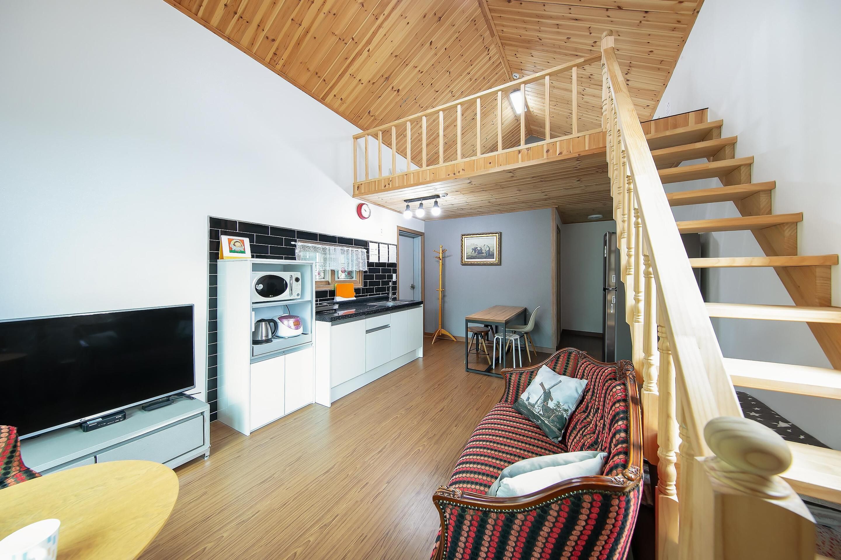 Un espacio habitable moderno con una escalera de madera, un televisor de pantalla plana, una cocina con cafetera y una zona de estar acogedora.