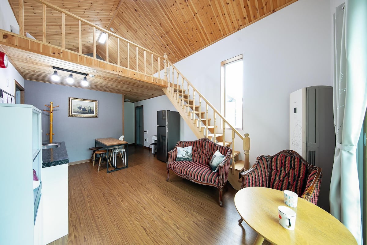 A spacious living area with a wooden staircase, a dining table, and a sofa.