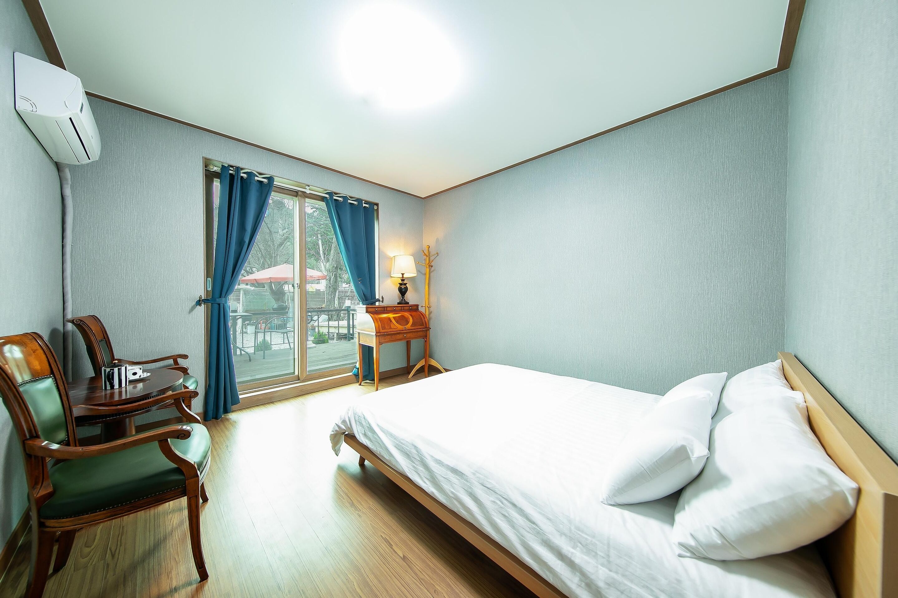 A hotel room with a bed, a desk with a chair, a lamp, and a window with curtains.