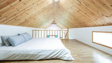 A bedroom with a sloped wooden ceiling, a bed with white bedding, and a large window on the right.