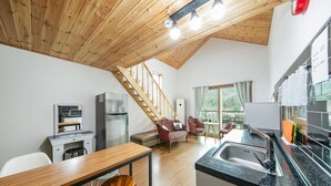 A modern kitchen with a wooden ceiling, a dining area with a wooden table and chairs, a sofa, and a staircase leading to an upper level. - Gapyeong Twelve Pension (Gapyeong)