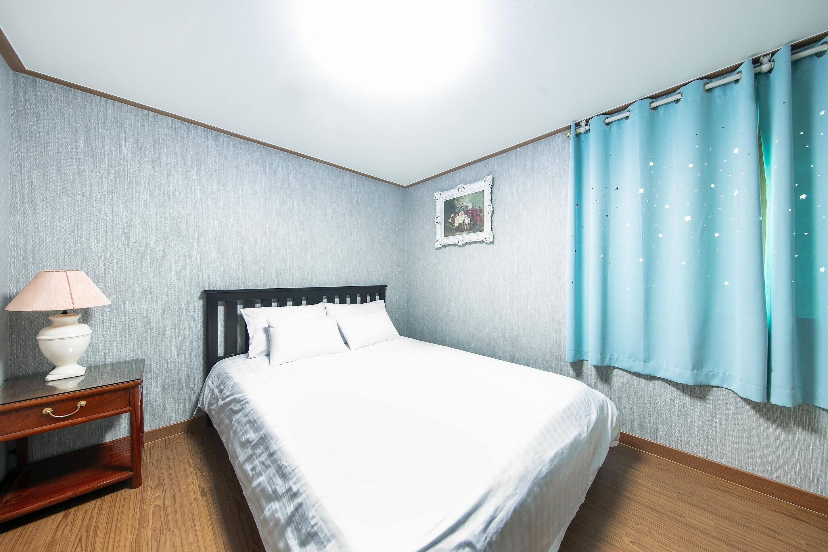 A neatly arranged bedroom with a bed, bedside table, lamp, and a framed picture on the wall.