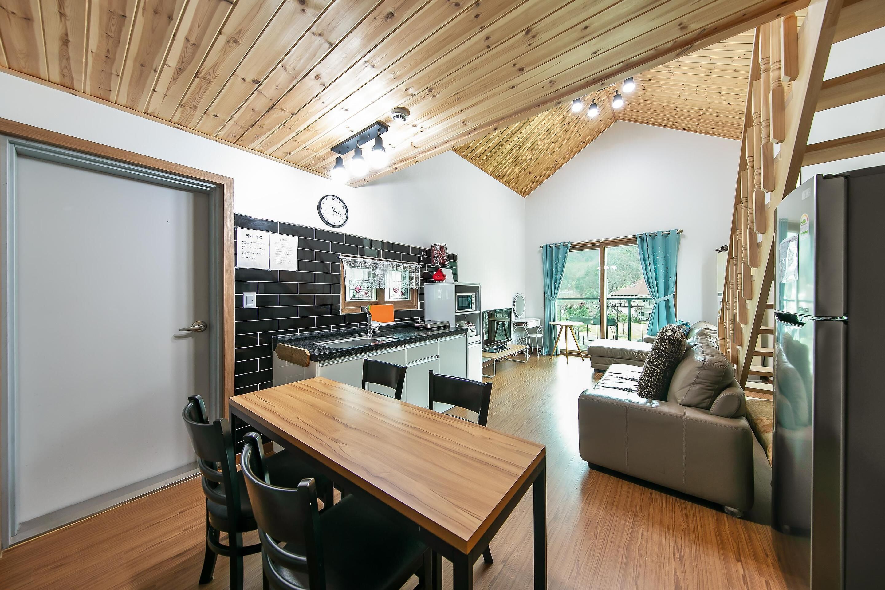Une cuisine moderne avec un mur recouvert de carreaux noirs, un plafond en bois et un coin repas comprenant une table et des chaises en bois.