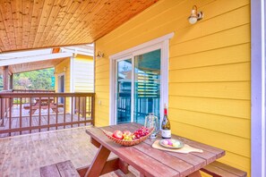 Una terraza de madera con mesas de picnic, una cesta de fruta, una botella de vino y una jarrón.