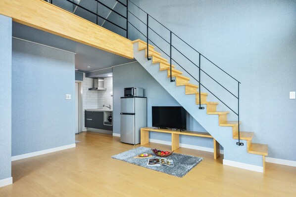 A modern living space with a wooden staircase, a kitchen area, and a dining area with a rug. - Namhae Haru Pension (Namhae)