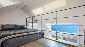 Une chambre avec un grand lit, une vue sur la mer par une fenêtre et une lucarne.