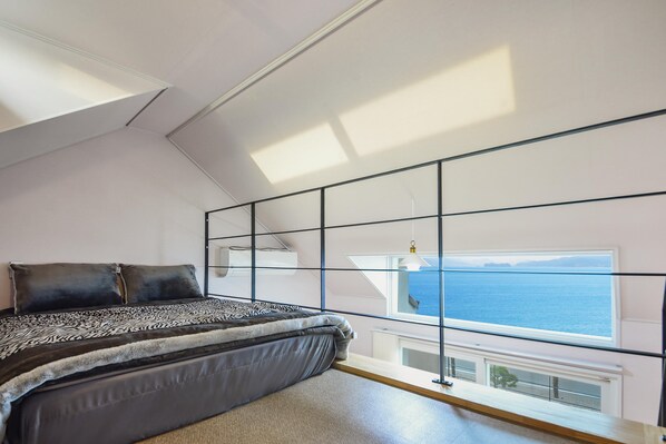A bedroom with a large bed, a view of the sea through a window, and a skylight. - Namhae Haru Pension (Namhae)