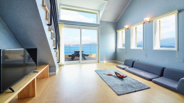 Un salon moderne doté d’un téléviseur, d’un canapé et offrant une vue sur la mer grâce à de grandes fenêtres.