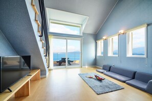 A modern living room with a TV, sofa, and a view of the sea through large windows. - Namhae Haru Pension (Namhae)