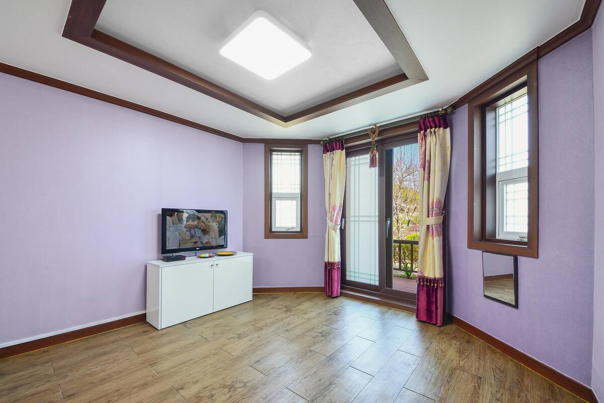 A room with a white cabinet, a flat-screen TV, and a large window with curtains.