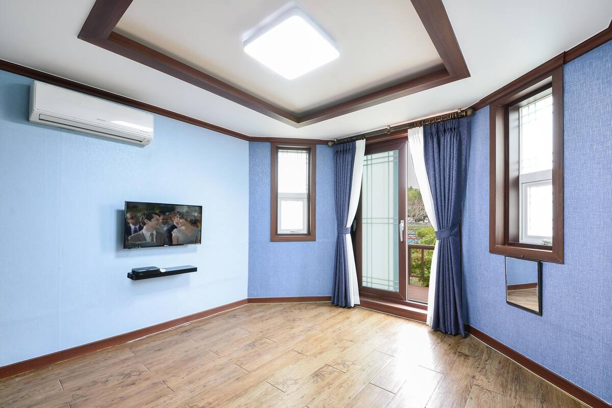 A room with a wooden floor, blue walls, a mounted TV, and a ceiling light.