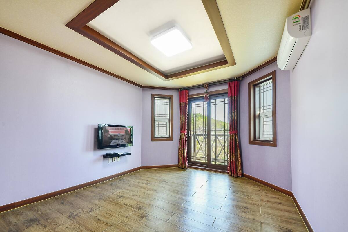 A room with a wooden floor, a flat-screen TV mounted on the wall, and a ceiling light fixture.